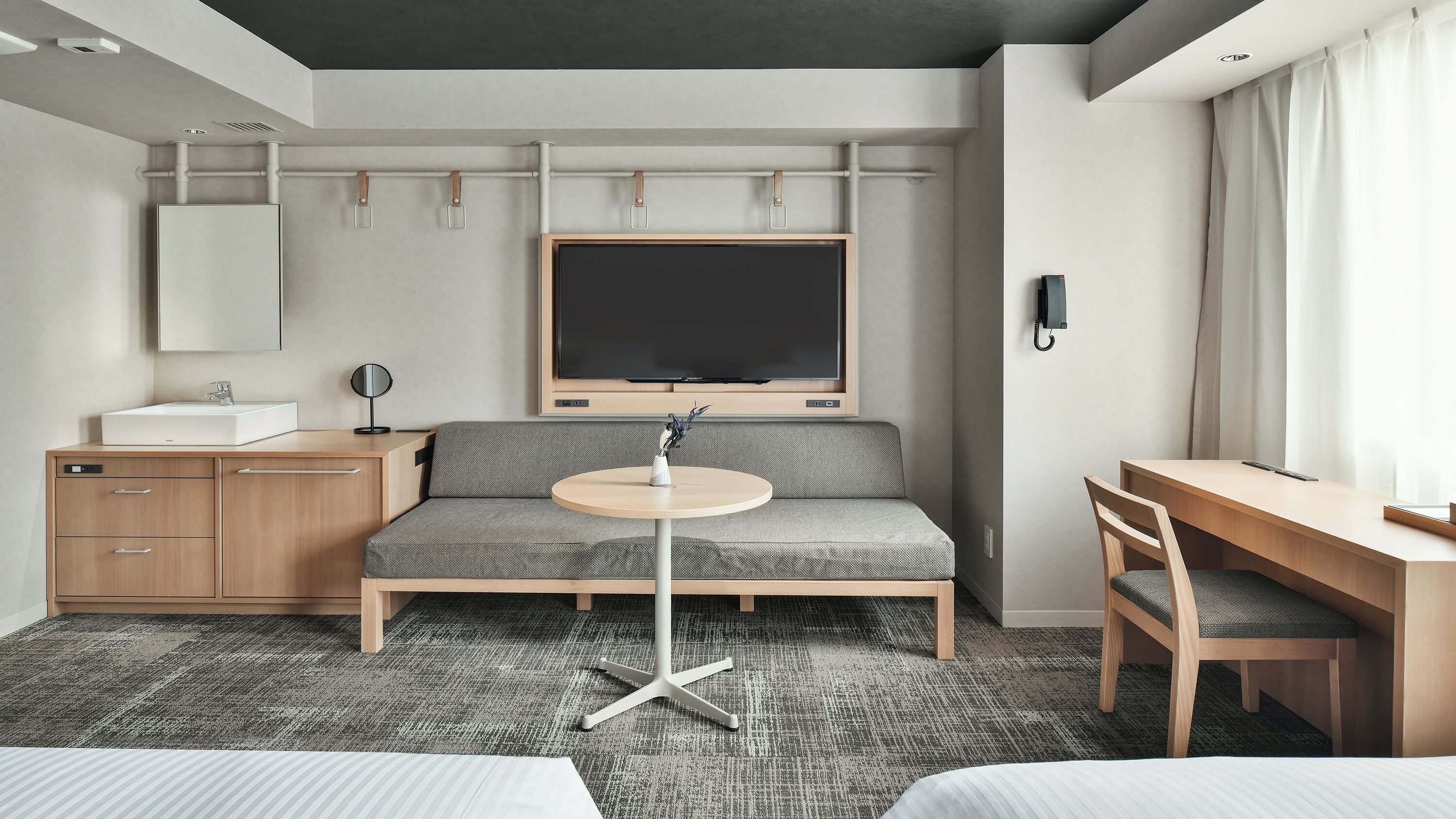 A modern hotel room with a sofa, a desk, a round table, a TV, a mirror, and a phone.