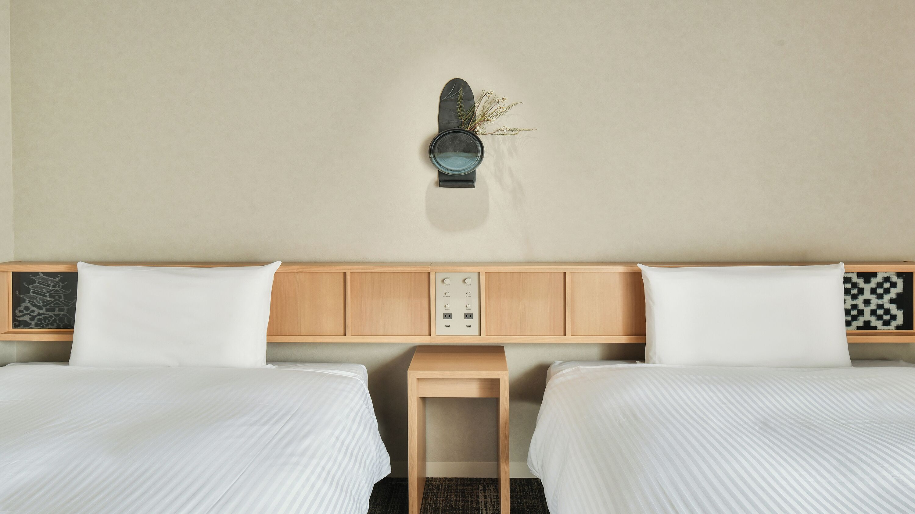 Habitación de hotel con dos camas, cabecero de madera, una mesita de noche de madera y una lámpara de pared.
