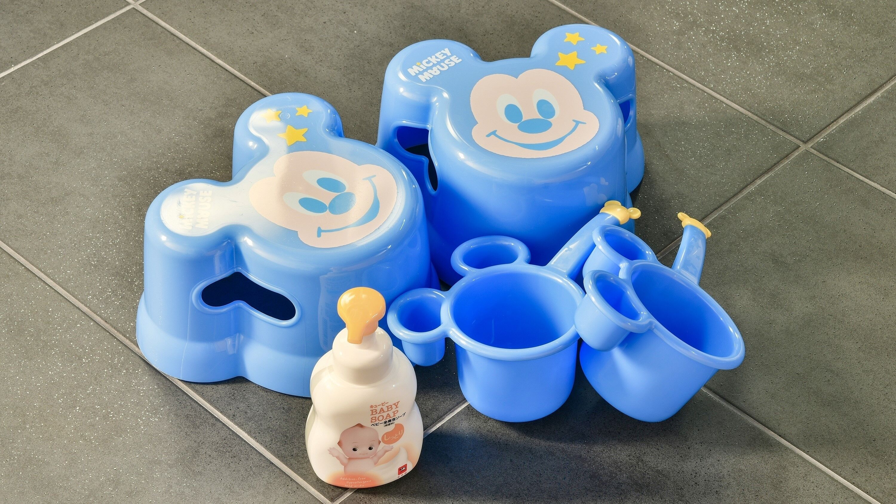 A Mickey Mouse themed baby bath set on a tiled floor.