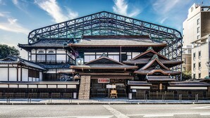 Um edifício japonês tradicional com uma estrutura de vidro moderna no topo, rodeado por outras construções tradicionais.