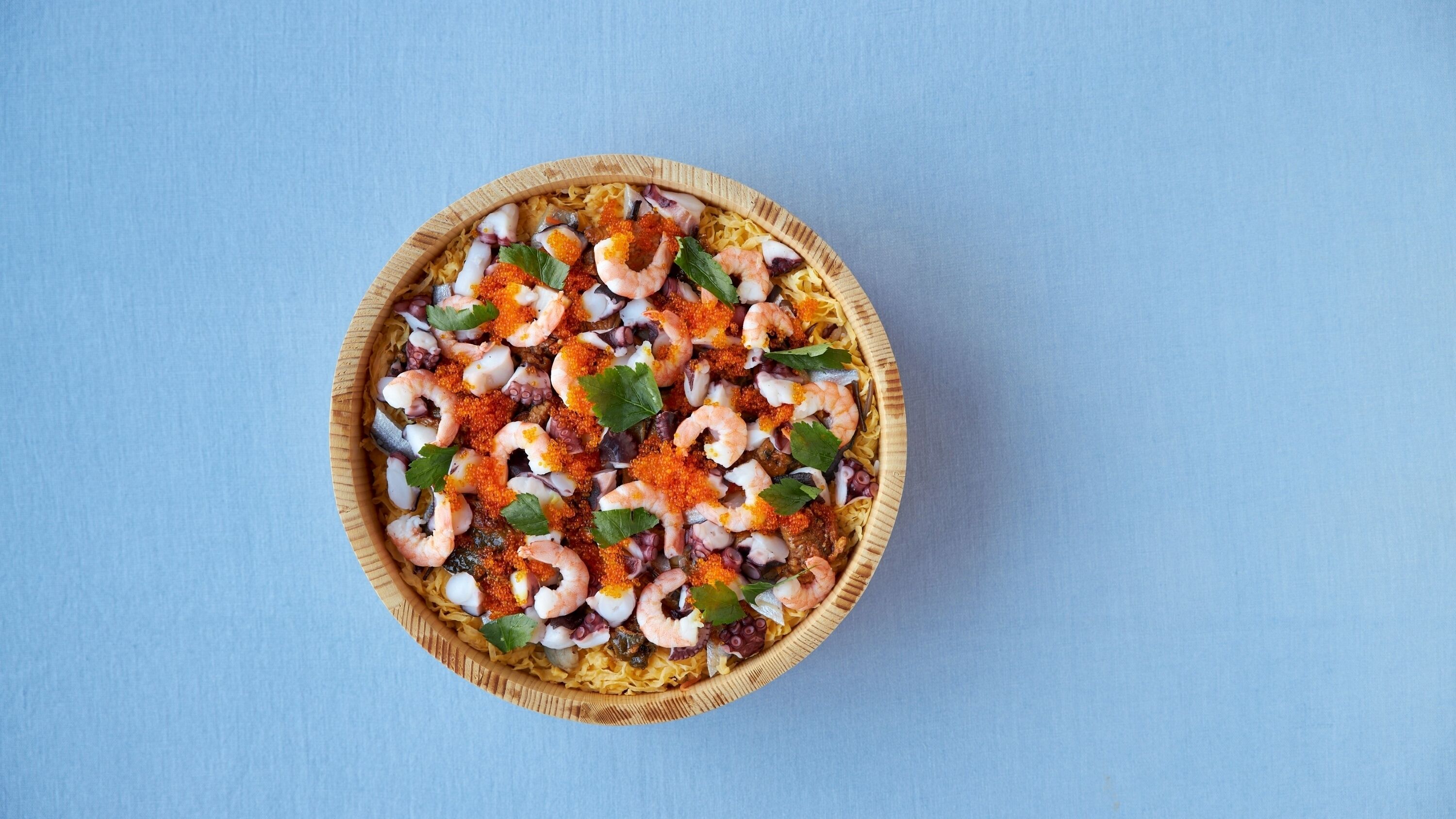 A wooden bowl filled with seafood salad on a blue background.