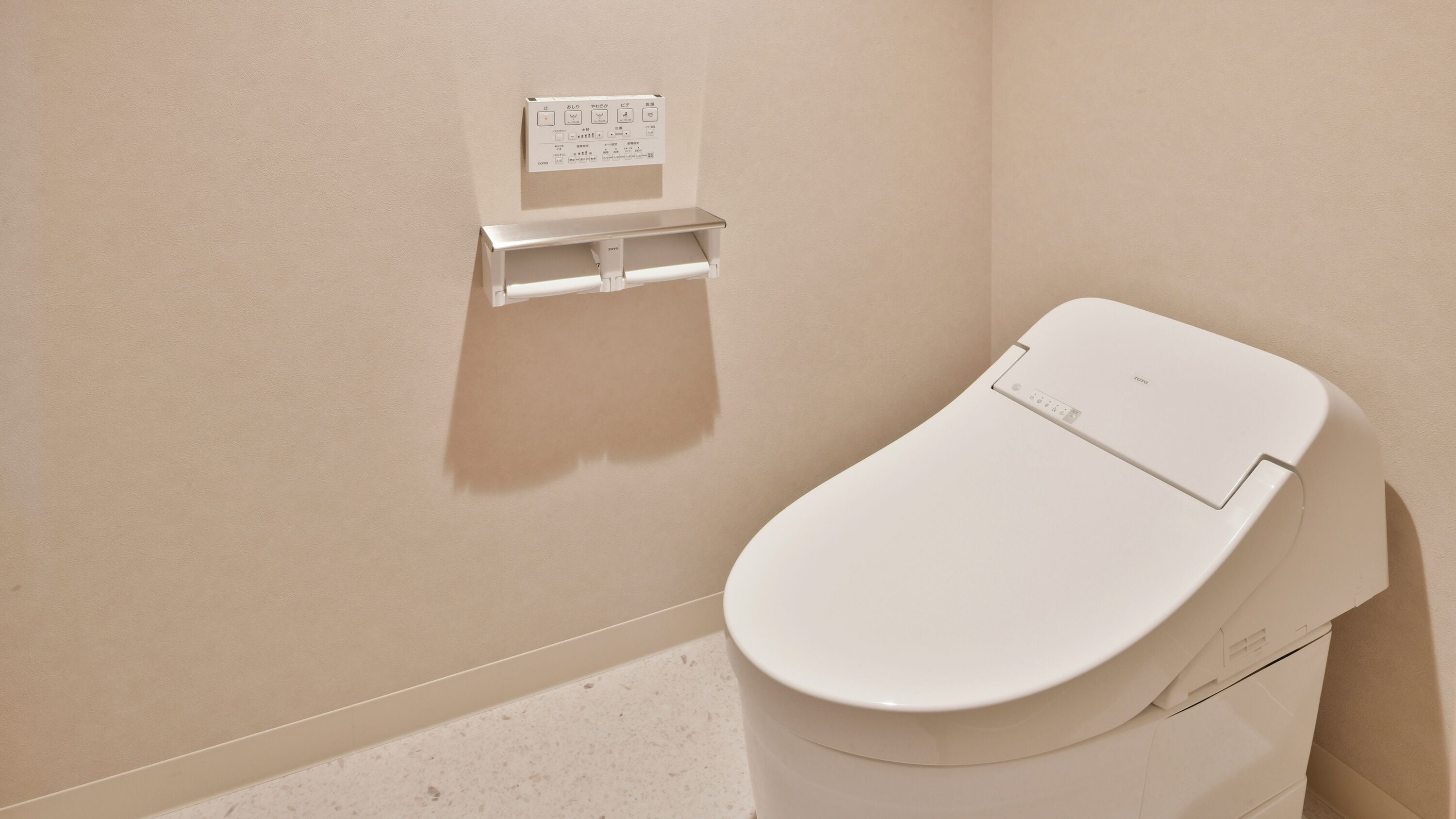 A modern toilet with a control panel and a toilet paper holder on the wall.