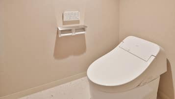 A modern toilet with a control panel and a toilet paper holder on the wall.