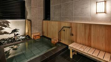 A modern spa area with a wooden bench, a small wooden stool, a bamboo screen, and a glass-enclosed hot tub.