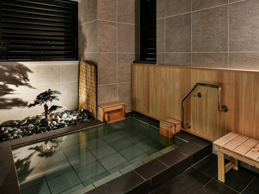 A modern spa area with a wooden bench, a small wooden stool, a bamboo screen, and a glass-enclosed hot tub.