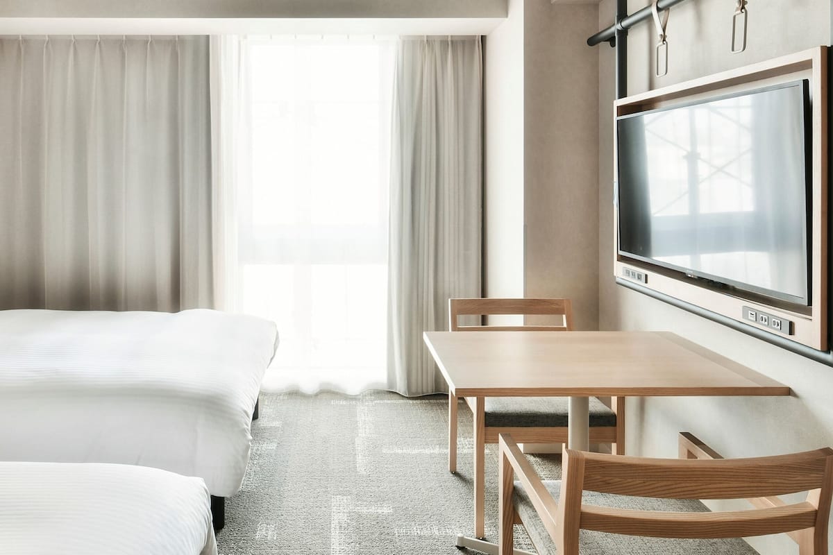 A hotel room with a bed, a desk, a chair, and a TV.