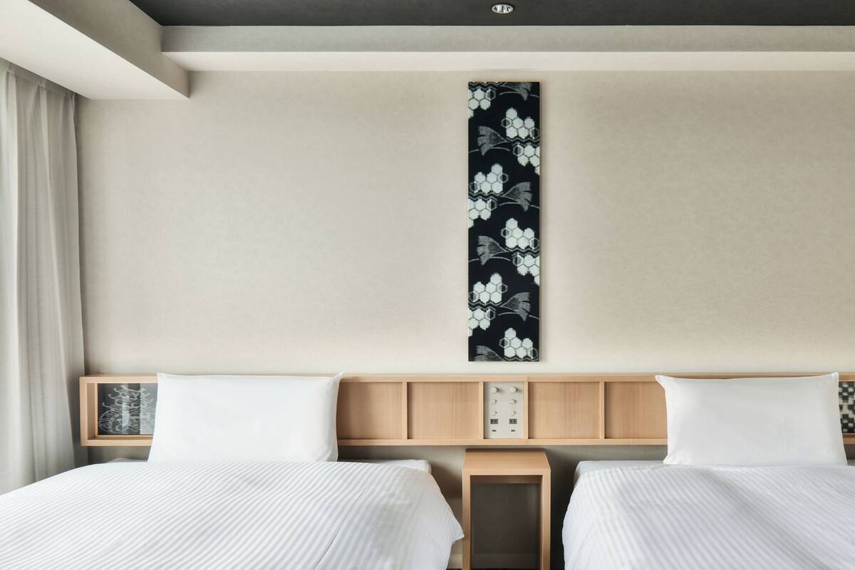 A hotel room with two beds, a wooden headboard, a wall-mounted artwork, and bedside tables with decorative items.