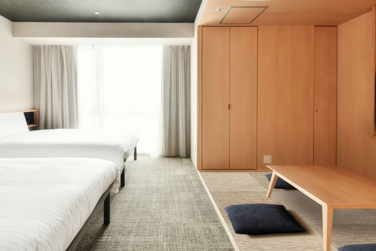 A hotel room with two beds, a wooden wardrobe, a desk, and a television.
