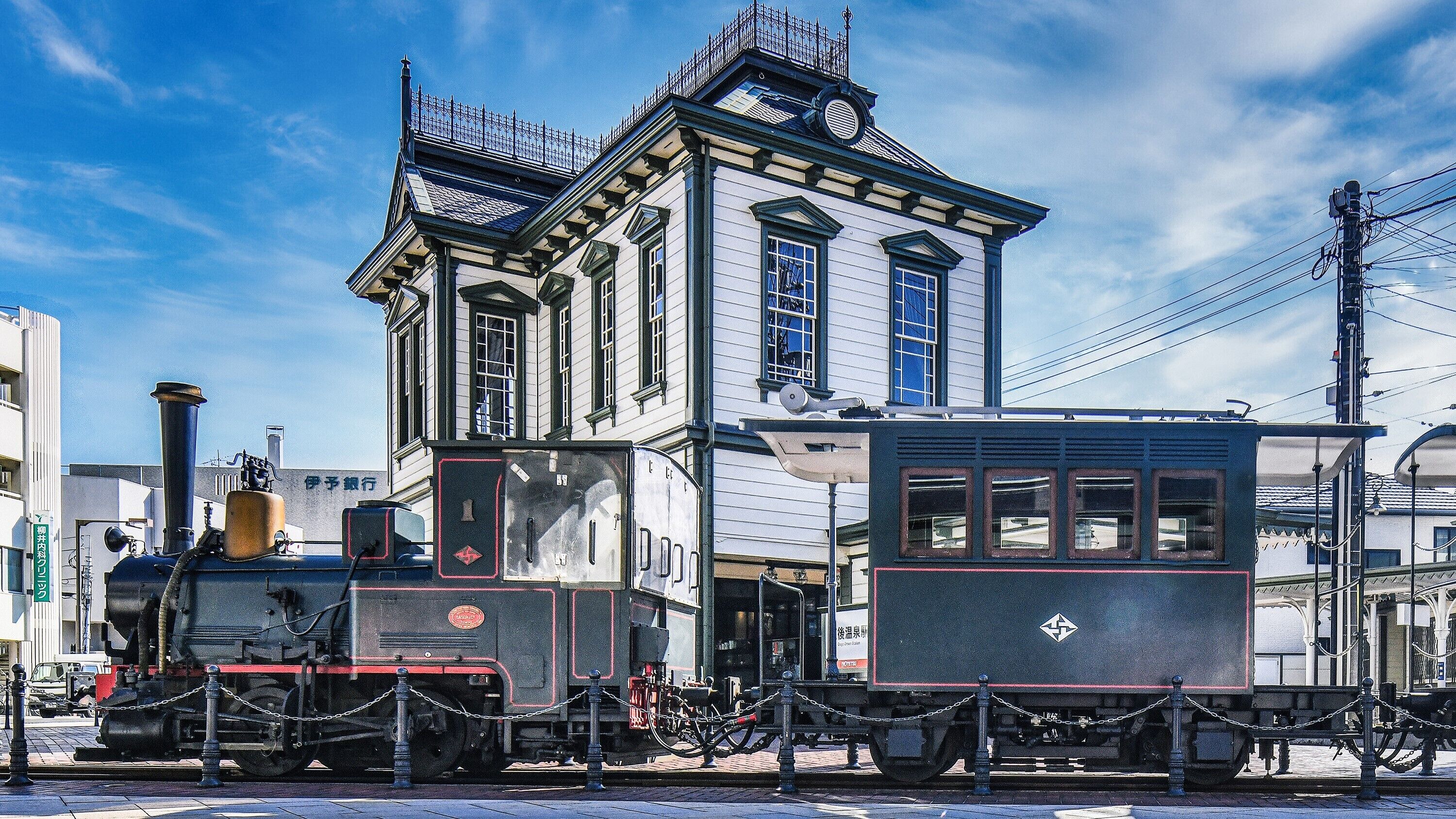 A historic building with a clock tower, a steam locomotive, and a vintage tram.