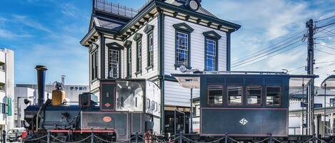 A historic building with a clock tower, a steam locomotive, and a vintage tram.