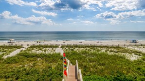 A beach with a wooden walkway leading to the shore, a flag, and a clear view of the ocean. - "Sandpiper Crossing" - Luxury Oceanfront Home, 4 Bedrooms / 3.5 Bathrooms (Holden Beach)