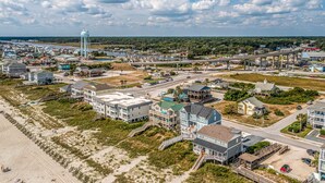 An aerial view of a coastal town with beachfront properties, a water tower, and a highway overpass. - "Sandpiper Crossing" - Luxury Oceanfront Home, 4 Bedrooms / 3.5 Bathrooms (Holden Beach)