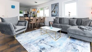 Ein modernes Wohnzimmer mit einem grauen Sofa, einem Couchtisch und einem Essbereich im Hintergrund.