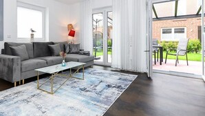 Ein modernes Wohnzimmer mit grauem Sofa, Couchtisch und Blick auf ein Backsteinhaus durch große Glasüren.