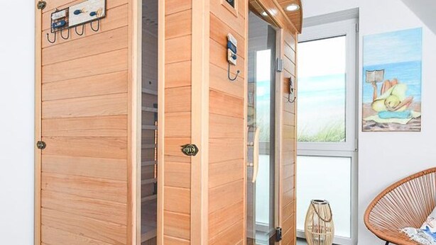 Eine Holzsauna mit Glastür, einem Korbsessel und einem Bild an der Wand.