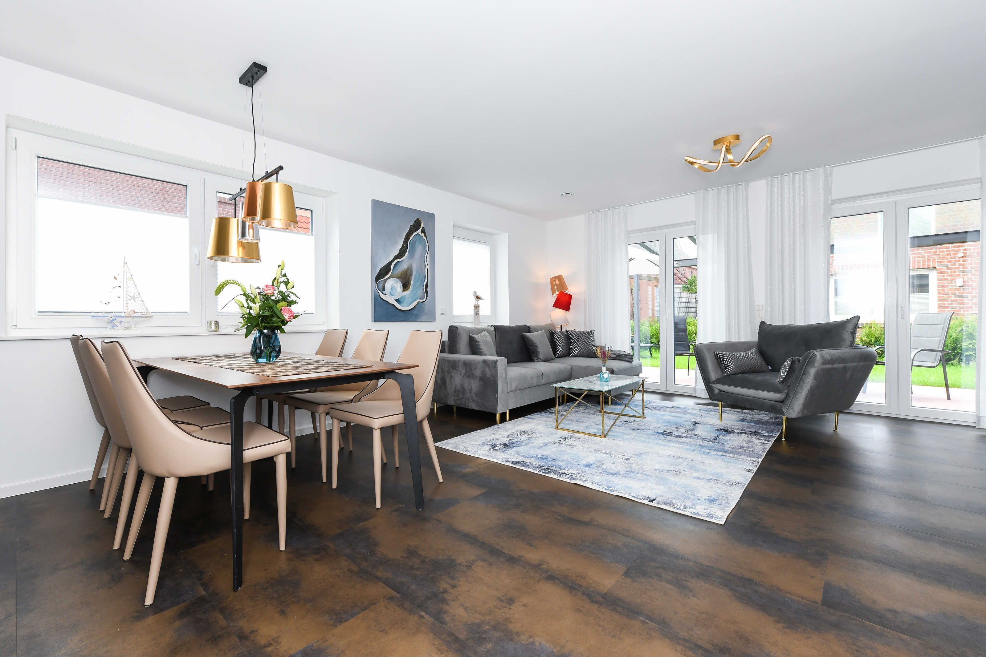Een moderne woonkamer met een eetgedeelte, een grijze bank en een zwarte fauteuil. Er is een groot raam met uitzicht op groen.