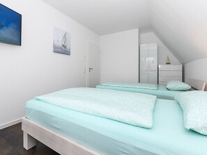 A bedroom with two beds, a white wardrobe, and a painting on the wall. - Vacation cottage Nordseeperle (Dornum)