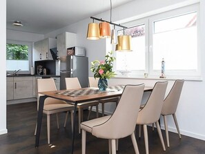A modern kitchen with a dining area, featuring a wooden table and chairs, a vase with flowers, and pendant lights. - Vacation cottage Nordseeperle (Dornum)