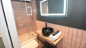 Ein Badezimmer mit einem modernen Waschbecken, einem Spiegel und einer Dusche.