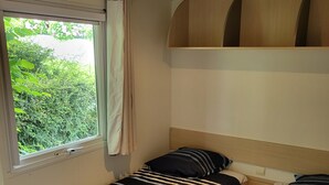 A bedroom with two single beds, a window with a curtain, and a built-in shelf above the beds. - Mobilhome Betzula 3ch (Larrau)