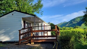 A small, single-story cabin with a wooden deck and a satellite dish. - Mobilhome Betzula 3ch (Larrau)