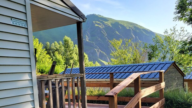 A wooden deck leading to a building with a metal roof, surrounded by natural scenery and mountains. - Mobilhome Betzula 3ch (Larrau)