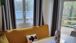 A modern, well-lit room with a yellow sofa, a wooden table, and a view of a garden through a large window. - Mobilhome Betzula 3ch (Larrau)