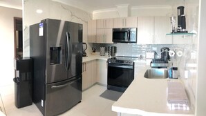 Una cocina moderna con electrodomésticos de acero inoxidable, armarios de colores claros y una repisa de vidrio.