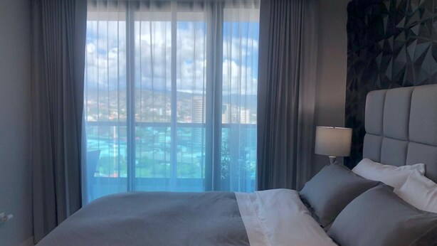 Habitación de hotel con una cama grande, vistas de la ciudad a través de ventanales del suelo al techo y un cabecero moderno.