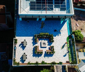 An aerial view of a modern building with a rooftop garden, a geometric pattern of planters, and a large window with metal framing.