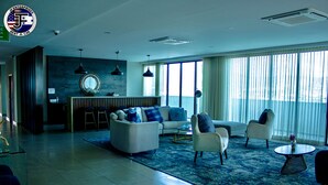 Una sala de estar moderna con un sofá, sillones y una mesa de centro. Hay un ventanal con cortinas, una pared de piedra y una lámpara colgante.