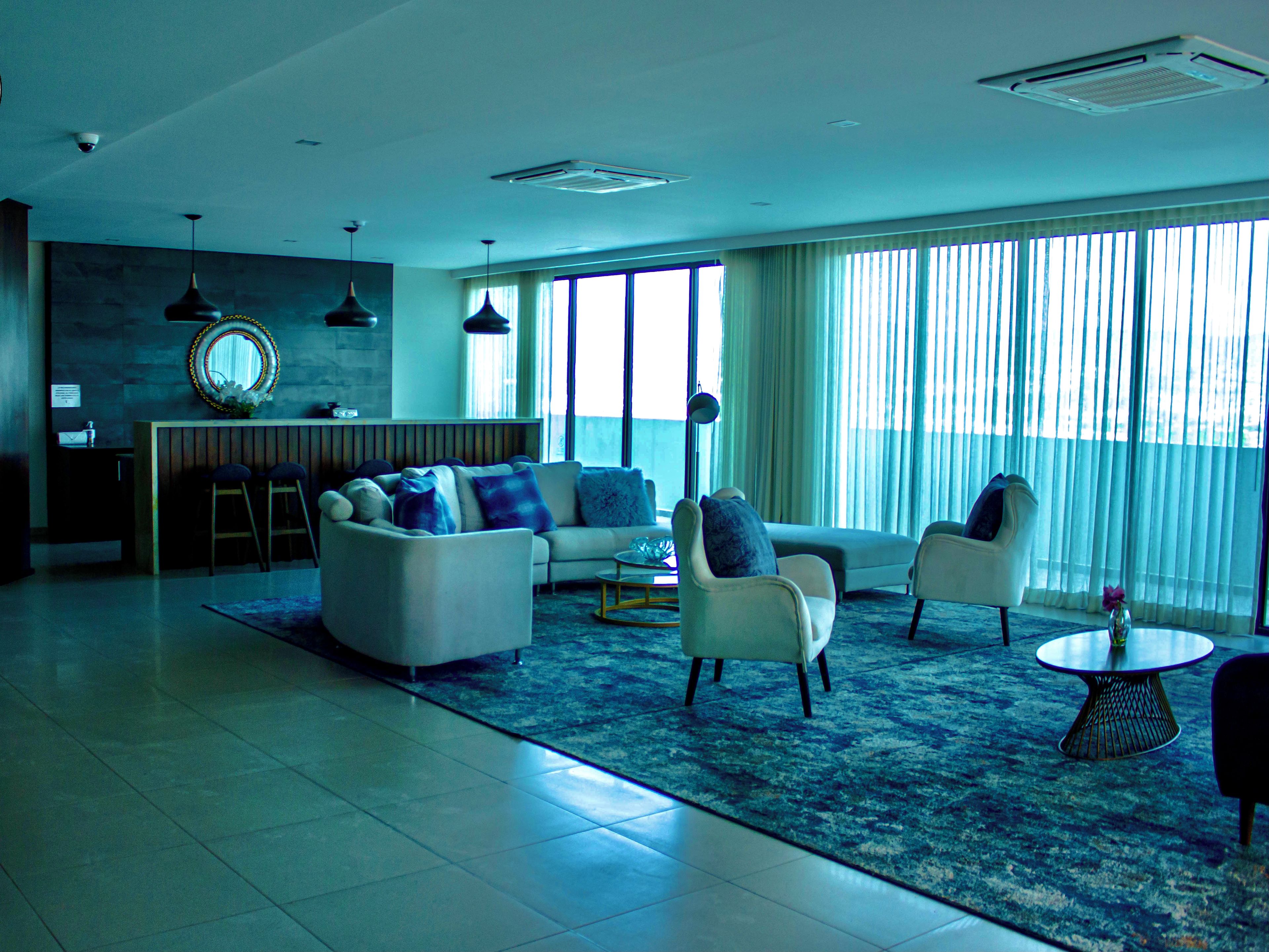 Una sala de estar moderna con un sofá, sillones y una mesa de centro. Hay un ventanal con cortinas, una pared de piedra y una lámpara colgante.