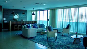 Una sala de estar moderna con un sofá, sillones y una mesa de centro. Hay un ventanal con cortinas, una pared de piedra y una lámpara colgante.