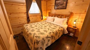 Un dormitorio de cabaña de madera con cama, mesita de noche, lámpara y ventana con cortinas.