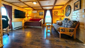 Interior de una cabaña de troncos con cama, sofá y televisor.