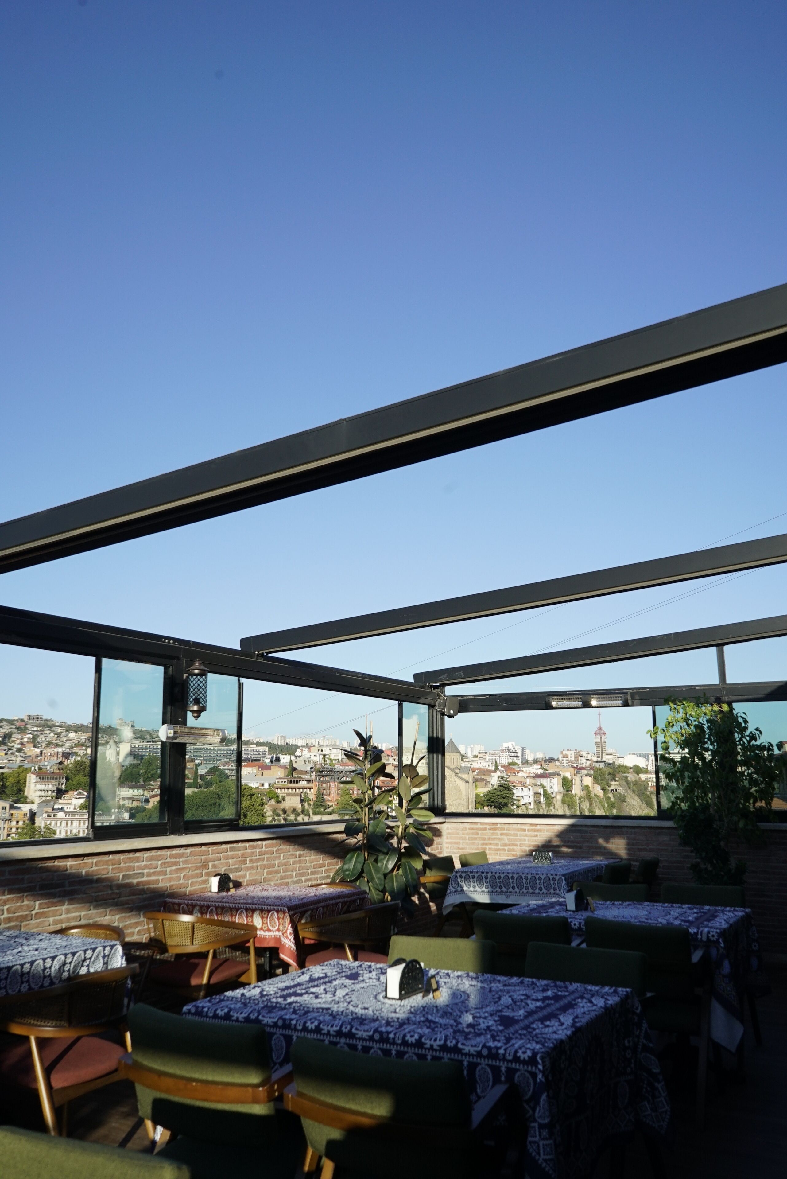 Un espace extérieur aménagé pour les repas, avec des tables et des chaises, offrant une vue sur le paysage urbain et un ciel bleu dégagé.