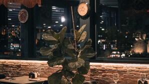 A restaurant with brick walls, large windows, and hanging decorations. Tables are set with wine glasses and plates. - Tbilisee Hotel (Tbilisi)
