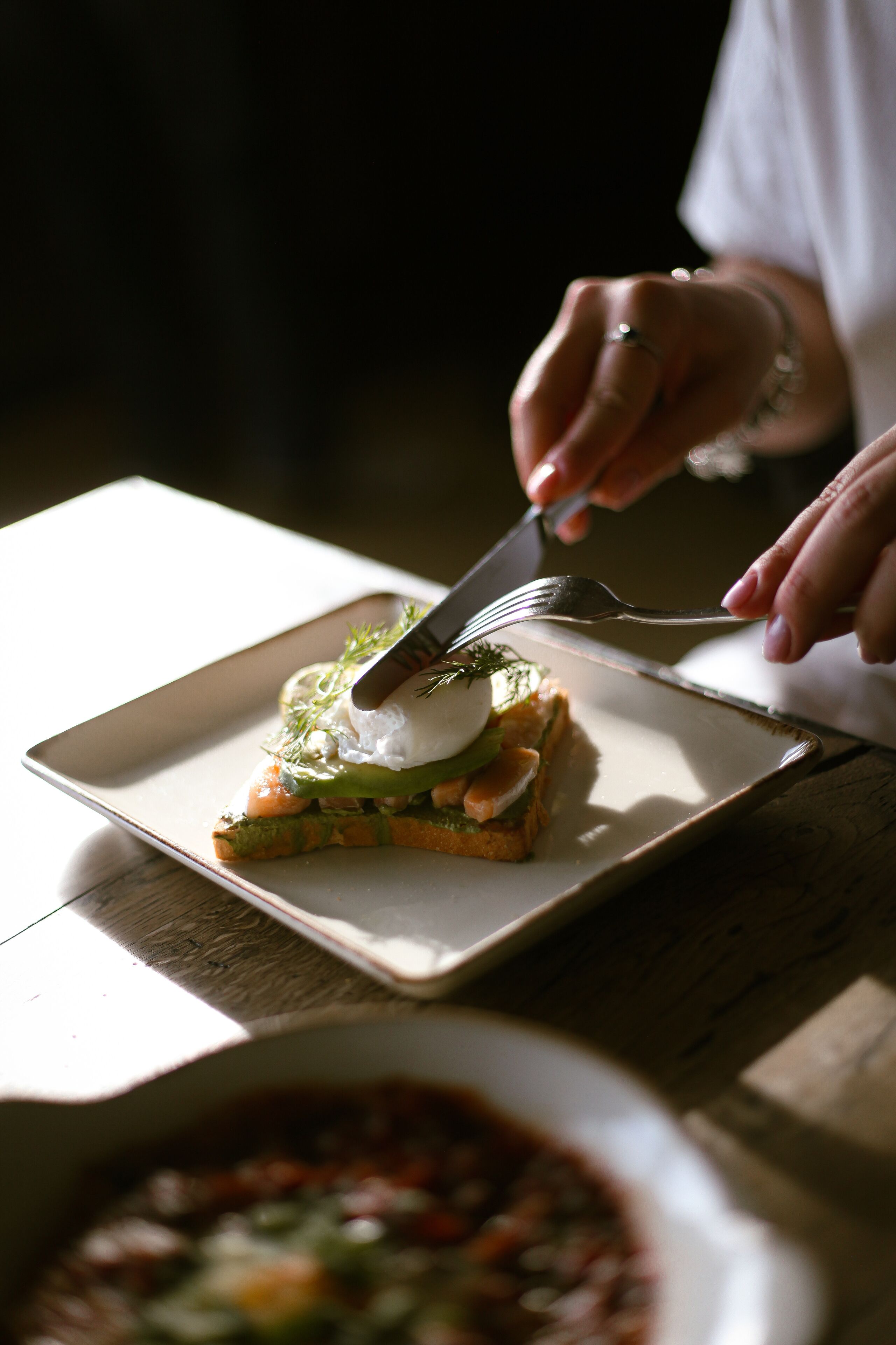 A person using a fork and knife to eat a sandwich on a square plate.