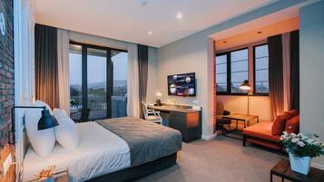 A hotel room with a large bed, a desk, a sofa, and a TV.