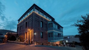 A modern building with a brick facade and large windows, featuring a well-lit entrance and outdoor seating area. - Tbilisee Hotel (Tbilisi)