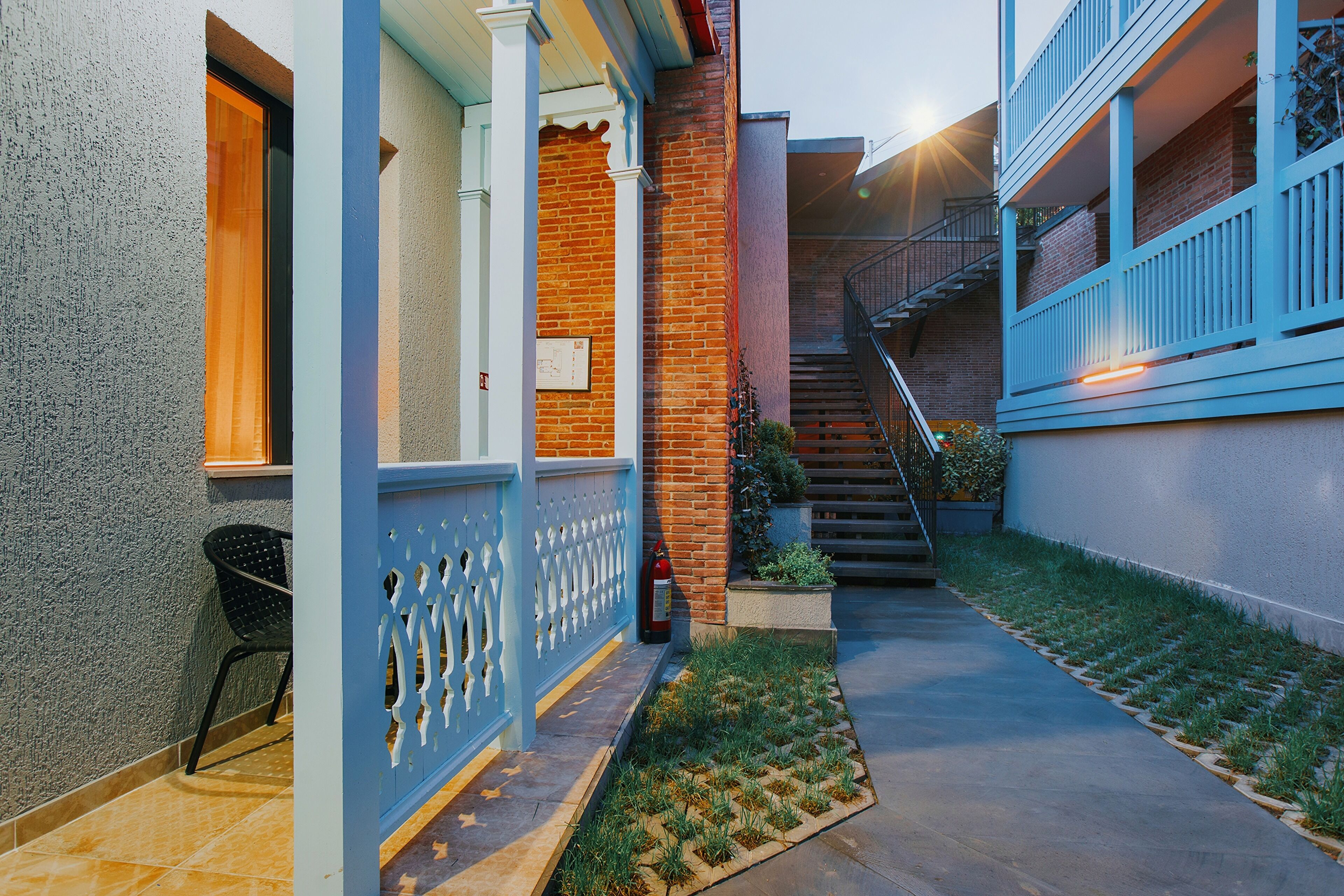 A residential building with a brick facade, a blue balcony, and a small garden area.