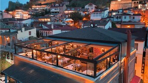 Un edificio moderno con un piso superior envuelto en vidrio, que cuenta con un comedor con mesas y sillas.