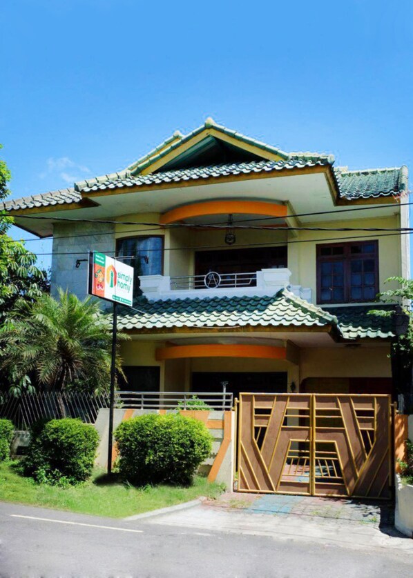 A two-story house with a tiled roof, a balcony, and a gated entrance.