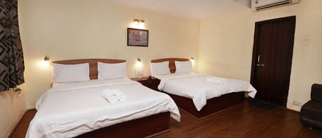 A hotel room with two beds, wooden flooring, a ceiling fan, and an air conditioning unit.