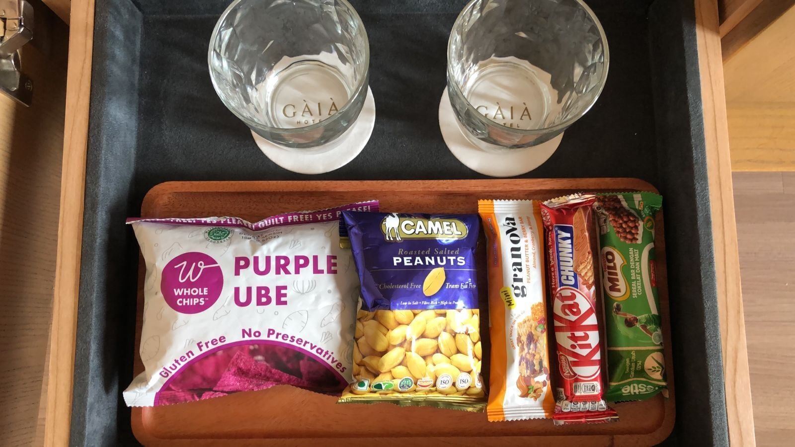Una bandeja con dos vasos de agua, una bolsa de chips Purple Hube, un paquete de cacahuates tostados con sal y una bolsita de Milo.