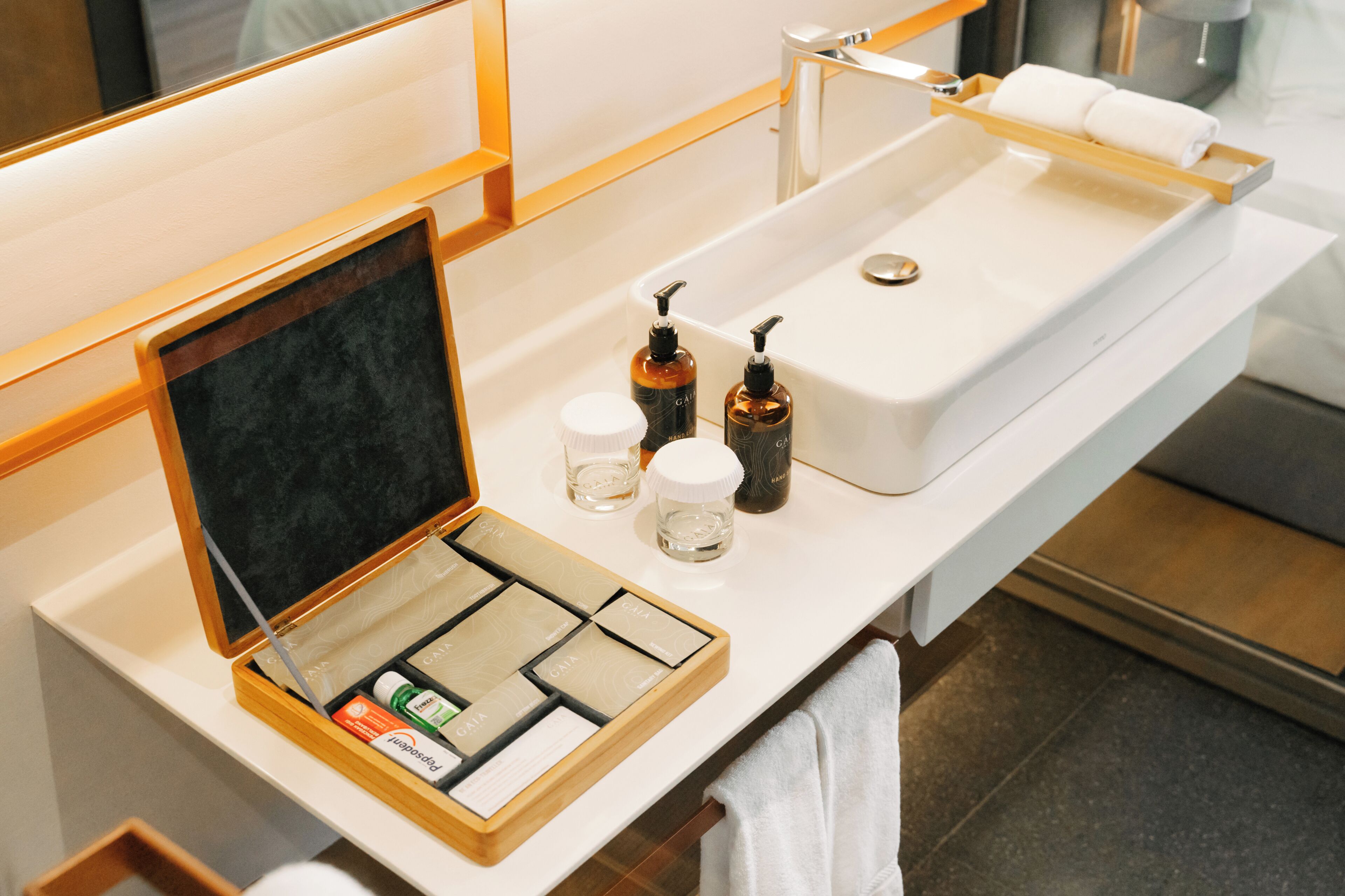 Een badkamer met een witte wastafel, een spiegel, een handdoekhouder en een schaaltje met toiletartikelen.