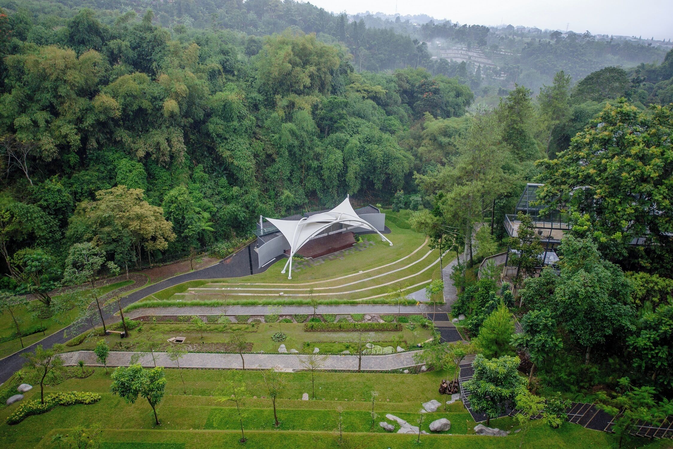 A modern building with a unique roof design surrounded by lush greenery and terraced gardens.