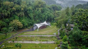 A modern building with a unique roof design surrounded by lush greenery and terraced gardens.