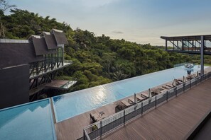 A rooftop infinity pool with wooden deck seating, surrounded by lush greenery and modern architecture. - The Gaia Hotel Bandung (Bandung)