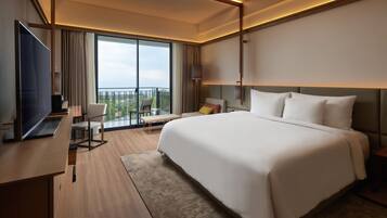 Une chambre d’hôtel moderne dotée d’un grand lit, d’un bureau avec un téléviseur à écran plat, d’une chaise et d’un balcon offrant une vue agréable.